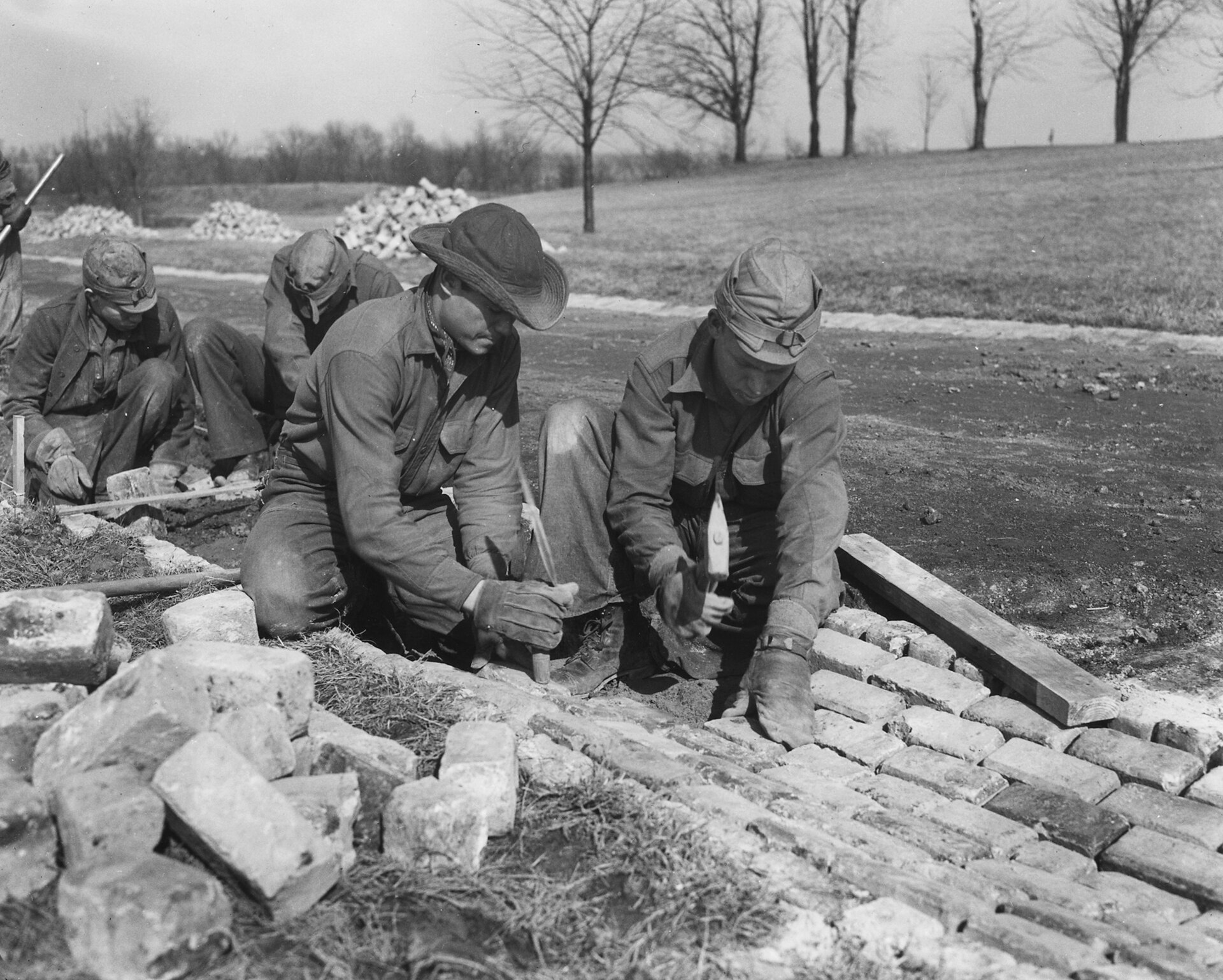 1933年、CCC（市民保全部隊）の隊員たちがレンガ舗装を行う。国家が直接雇用した若者は約300万人。その全員に作業着が必要だった（米国国立公文書館 NARA 所蔵／パブリックドメイン）